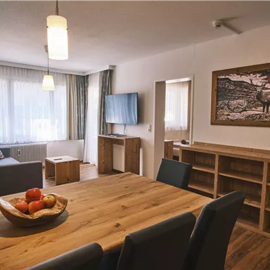 Ein modernes Wohnzimmer mit Holzverarbeitung und einer großen Fensterfront. Am Esstisch steht eine Schale mit frischen Äpfeln.