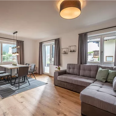 A bright and modern living room with a couch and a dining table. Large windows offer a view of the landscape.