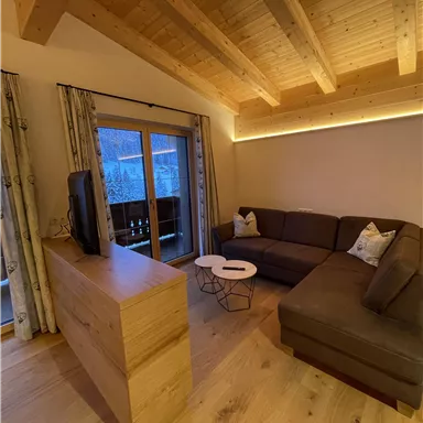 Ein modernes Wohnzimmer mit Holzdecken und einer gemütlichen Couch. Große Fenster bieten Blick auf die Natur und sorgen für viel Tageslicht.