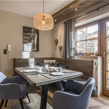 Ein einladender Essbereich mit einem Holztisch und gemütlichen Stühlen. Große Fenster bieten einen Blick nach draußen und lassen viel Tageslicht herein.