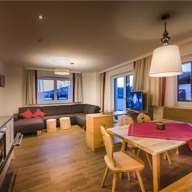 A modern living room with a cozy seating area, a dining area, and large windows. The space is bright and cheerfully designed.