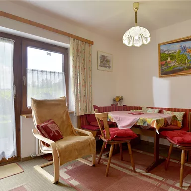 A cozy dining area with a table and chairs. The window lets in a lot of natural light and there is a beautiful painting on the wall.