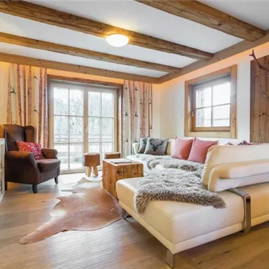 Ein modern eingerichtetes Wohnzimmer mit einer komfortablen Couch und einem Sessel. Große Fenster lassen viel Licht hereinfahren und schaffen eine gemütliche Atmosphäre.