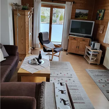 A cozy living room with a sofa, an armchair, and a television.  
Large windows provide plenty of daylight and a warm atmosphere.