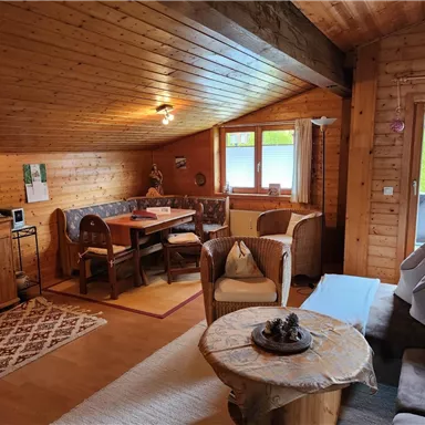 A cozy living space with wooden paneling and large windows. A dining table, comfortable armchairs, and a TV corner give the atmosphere a warm character.