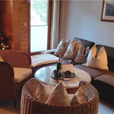 A cozy living space with a large sofa and wicker chairs. In the background, there is a Christmas tree, festively decorated.