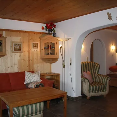 Ein gemütliches Wohnzimmer mit einem roten Sofa und einem Holztisch. Die Wände sind teilweise aus Holz, und es gibt eine gemütliche Sitzecke mit einem Sessel.