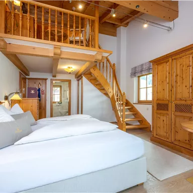 Ein gemütliches Zimmer mit einem Doppelbett und Sicht auf eine Veranda. Holzdecken und -möbel schaffen eine warme Atmosphäre.