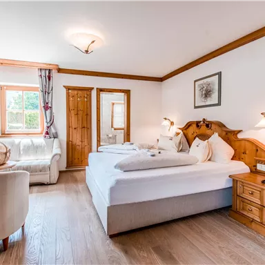 Ein gemütliches Schlafzimmer mit einem großen Bett und Holzdetails. Das Zimmer verfügt über ein Fenster, einen Sessel und einen Nachttisch.