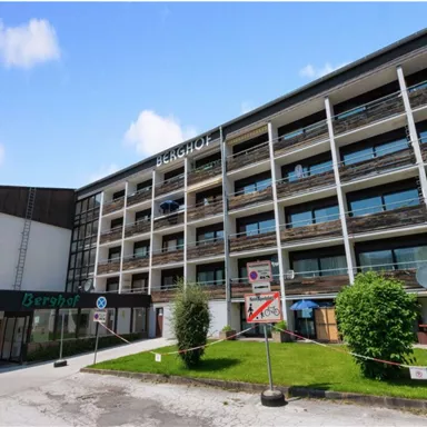 A modern hotel building with several floors and large windows. In front of the building, there is a well-maintained green area.