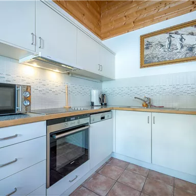 Eine moderne Küche mit weißen Schränken und Holzdetails. Sie ist ausgestattet mit einem Mikrowellenherd und einem Backofen.