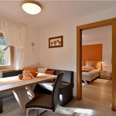 A cozy living space with a dining area and an adjacent bedroom. Bright colors and plenty of daylight create an inviting atmosphere.