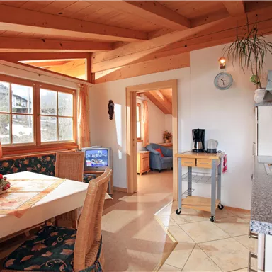 A cozy kitchen with wooden elements and large windows. The dining area is bright and inviting, perfect for shared meals.