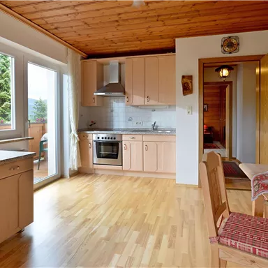 A bright kitchen with wooden cabinets and a dining table. The view from the window shows a beautiful mountain landscape.