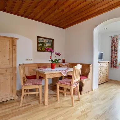 A cozy dining area with a table and wooden chairs. In the background, there is a sideboard and a window with a view outside.