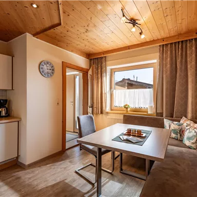 A cozy kitchen with a dining table and a bench. Large windows provide plenty of daylight.