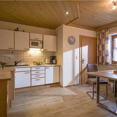 A modern kitchen unit with white cabinets and a wooden ceiling. The room is bright and inviting, with a dining table and chairs.