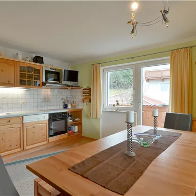 Eine gemütliche Küche mit Holzschränken und einer Essgruppe. Das Fenster bietet einen Blick ins Freie und lässt viel Licht herein.