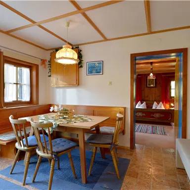 Ein gemütlicher Essbereich mit einem Holztisch und Stühlen. Im Hintergrund ist ein weiterer Raum sichtbar, der einladend wirkt.