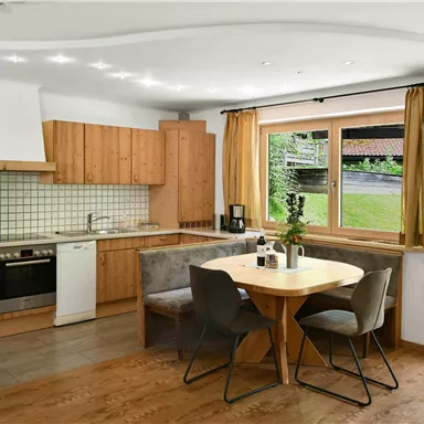 Eine moderne Küche mit Holzschränken und einem runden Esstisch. Große Fenster bieten Blick auf den Garten.