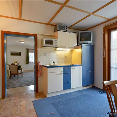 Eine helle Küche mit blauen Schränken und modernen Geräten. Im Hintergrund befindet sich ein Essbereich mit einem Tisch und Stühlen.