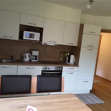 Eine moderne Küche mit Holz- und weißen Schränken. Der Essbereich besteht aus einem Tisch und zwei Stühlen.