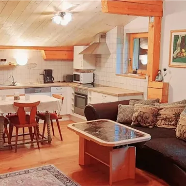A cozy living kitchen with a wooden ceiling and modern furnishings. The room is bright and inviting, with a sofa and a dining table for four people.