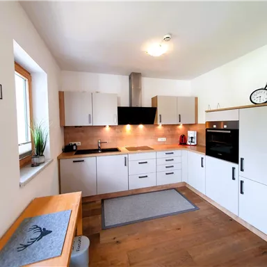 A modern kitchen with white cabinets and wood details. The room is bright and well-equipped, perfect for cooking.