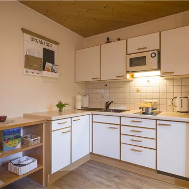 A modern kitchen with white cabinets and a wooden ceiling. It is well-equipped with a stove, a microwave, and a refrigerator.