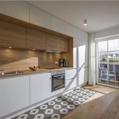 A modern kitchen with wooden shelves and white cabinets. The room has large windows that let in plenty of daylight.