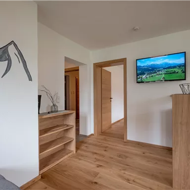 A modern living room with wooden shelves and a TV wall. On the wall, there is an artistic depiction of a mountain.