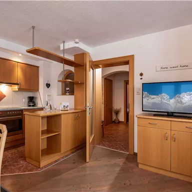 A modern kitchen with wooden cabinets and a television. The room is bright and inviting with a dining area.