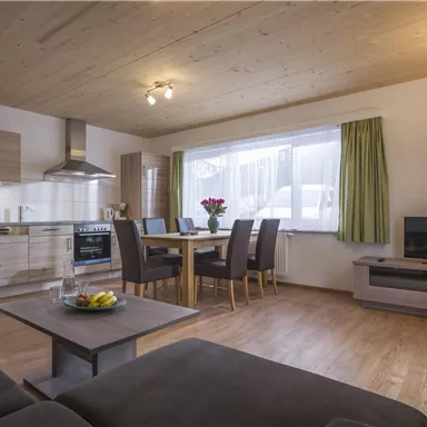 Eine moderne Küche mit einem Essbereich und einem gemütlichen Wohnzimmer. Große Fenster lassen viel Licht herein und sorgen für eine einladende Atmosphäre.