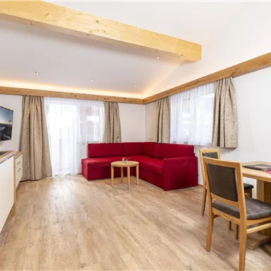 Eine moderne Wohnung mit Holzdecke und großen Fenstern. Sie verfügt über eine gemütliche Sitzecke, einen Esstisch und eine Küchenzeile.