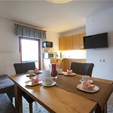 Ein gemütlicher Essbereich mit einem Holztisch und Stühlen. Die offene Küche ist modern eingerichtet und gut beleuchtet.