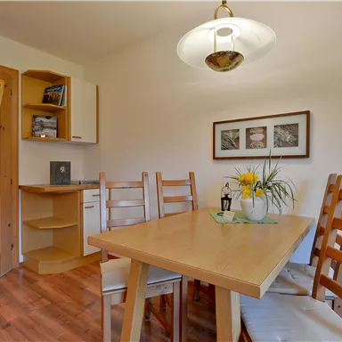 Ein gemütlicher Essbereich mit einem Holztisch und Stühlen. Die Wände sind hell, und es gibt eine schöne Blumendekoration auf dem Tisch.