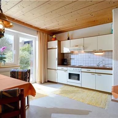 Eine helle Küche mit modernem Design und einem Essbereich. Große Fenster sorgen für viel Tageslicht.