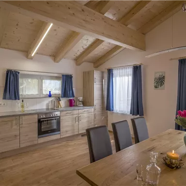 Eine moderne Küche mit Holzdecke und großen Fenstern. Am Tisch stehen frische Blumen und Kerzen.