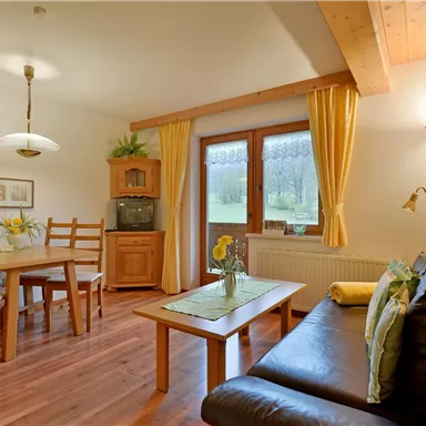 Eine gemütliche Wohnküche mit Holzmöbeln und einem großen Fenster. Der Raum ist hell und freundlich gestaltet.