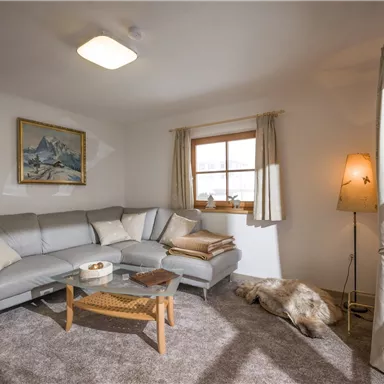 A cozy living room with a gray sofa and a small table. A window lets in plenty of daylight and there is a relaxed atmosphere.
