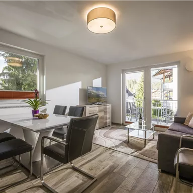 A modern living room with a cozy couch and a dining area.  
Large windows provide plenty of daylight and a view of the outdoors.
