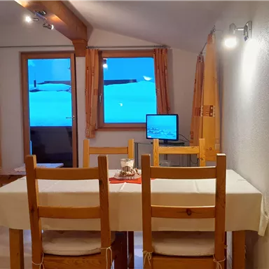 A cozy living space with a dining table and chairs. Blue light is shining through the window, indicating a wintry environment.