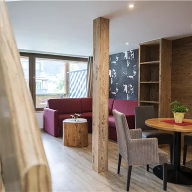 Ein modernes Wohnzimmer mit Holzverkleidung und einem gemütlichen roten Sofa. Ein runder Tisch und Stühle laden zum Verweilen ein.