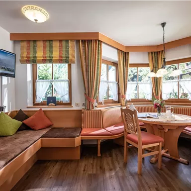 A cozy dining area with a round table and wooden bench. Large windows provide plenty of daylight and an inviting atmosphere.