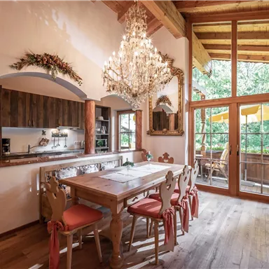 An elegant dining room with a large wooden table and stylish chairs. Large windows offer a view of a green environment and plenty of daylight.