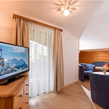 A cozy living space with a blue sofa and a television. Large windows let in plenty of natural light.