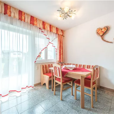 A bright dining room with a table and chairs. The walls are decorated with heart decor and large windows let in plenty of light.