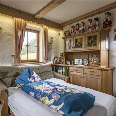 A cozy bedroom with a sofa bed and wooden furniture. Decorative figures and flower arrangements stand on the wall.