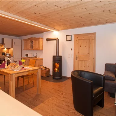 A cozy living space with a wooden ceiling and a modern fireplace. A dining area and a kitchen are also visible, the warm atmosphere invites you to relax.