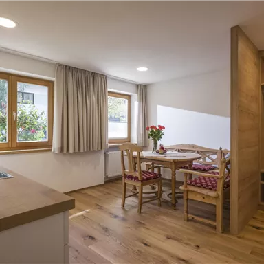 Eine gemütliche Küche mit einem kleinen Essbereich und großen Fenstern. Der Boden ist aus Holz und es gibt frische Blumen auf dem Tisch.